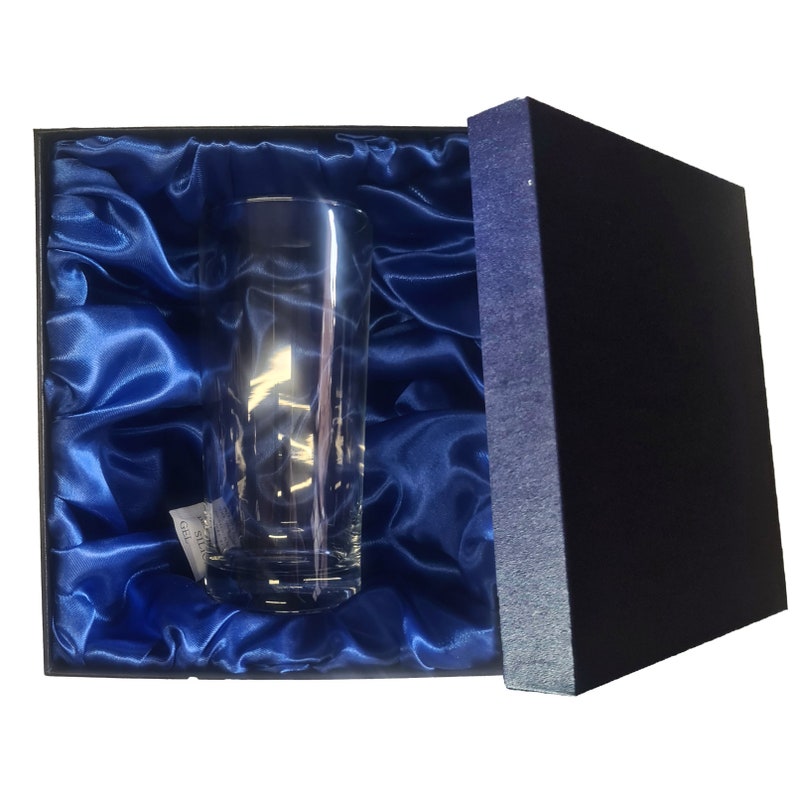 May include: A clear glass tumbler in a blue satin-lined box. The box is open and the glass is visible.