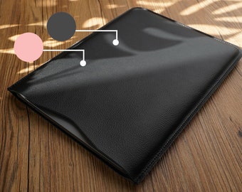 Könnte beinhalten: Eine schwarze Lederhülle für Laptops mit einer dezenten, strukturierten Oberfläche. Die Hülle liegt auf einer Holzoberfläche.