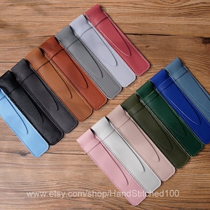 Könnte beinhalten: Sortiment von 12 Leder-Stift-Etuis in verschiedenen Farben, darunter Blau, Grün, Braun, Rosa und Grau. Die Etuis sind versetzt auf einer Holzoberfläche angeordnet. www.etsy.com/shop/HandStitched100