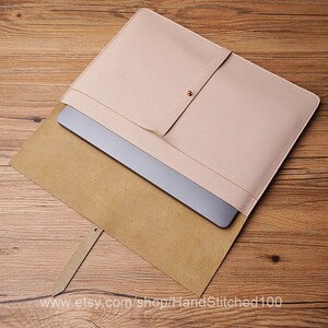 May include: A light pink leather laptop sleeve with a brown suede lining. The sleeve has a flap with a magnetic closure and a small pocket on the front.