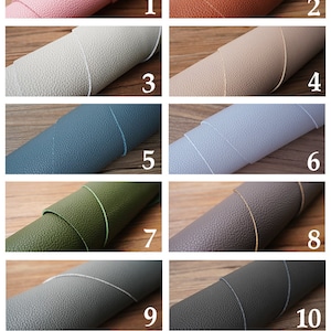 Op de afbeelding: Twaalf voorbeelden van echt leer in verschillende kleuren. Het leer is opgerold en de randen zijn zichtbaar. De kleuren zijn: roze, oranje, lichtgrijs, beige, blauw, lichtblauw, groen, grijs, donkergrijs, donkergroen en zwart.
