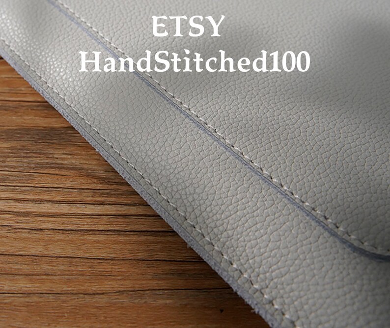 Puede incluir: Primer plano de un art&iacute;culo de cuero gris claro con costuras visibles. El texto "ETSY HandStitched100" est&aacute; impreso en blanco. El cuero tiene una superficie texturizada.