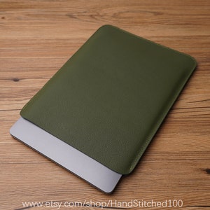 Op de afbeelding: Een groene leren laptophoes met een subtiele textuur. De hoes is gesloten en een laptop is gedeeltelijk zichtbaar van binnen.