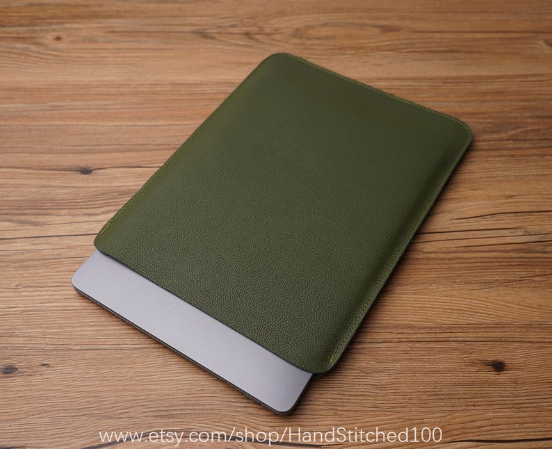Op de afbeelding: Een groene leren laptophoes met een subtiele textuur. De hoes is gesloten en een laptop is gedeeltelijk zichtbaar van binnen.