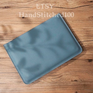 Op de afbeelding: Een lichtblauwe leren laptophuls. De hoes ligt plat op een houten oppervlak.