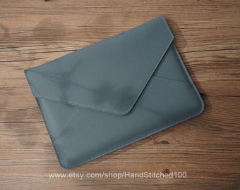 May include: A blue leather laptop sleeve with a flap closure. The sleeve is on a wooden surface.
