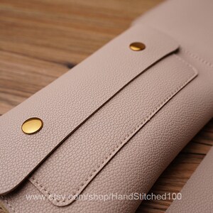 May include: A light pink leather wallet with a flap closure and gold-toned snaps. The wallet has a stitched detail and the text "www.etsy.com/shop/HandStitched100" is printed on the bottom.