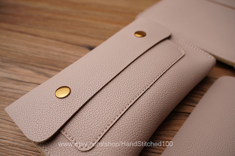 May include: A light pink leather wallet with a flap closure and gold-toned snaps. The wallet has a stitched detail and the text "www.etsy.com/shop/HandStitched100" is printed on the bottom.