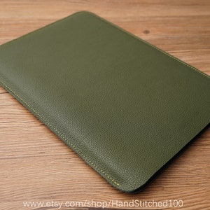 Op de afbeelding: Een groene leren laptophoes met gele stiksels. De hoes is gemaakt van gestructureerd leer en heeft een gladde, nette afwerking.