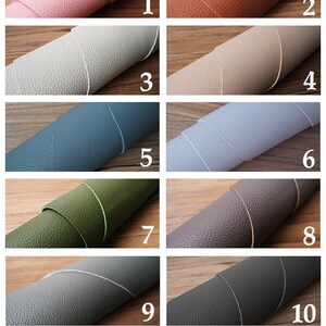 Op de afbeelding: Twaalf voorbeelden van echt leer in verschillende kleuren. Het leer is opgerold en de randen zijn zichtbaar. De kleuren zijn: roze, oranje, lichtgrijs, beige, blauw, lichtblauw, groen, grijs, donkergrijs, donkergroen en zwart.