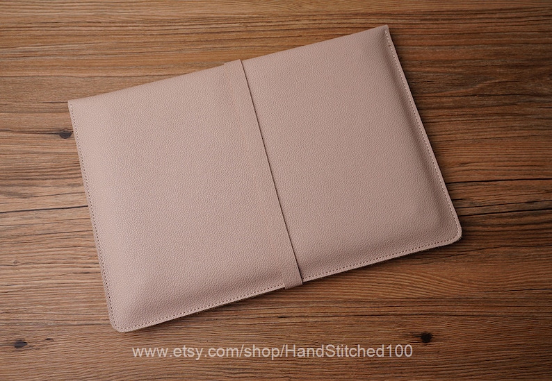 May include: A light pink leather laptop sleeve with a stitched seam down the center. The sleeve is lying on a wooden surface.