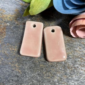 May include: Two rectangular ceramic tiles with a light pink glaze and a hole in the top. The tiles are smooth and glossy.