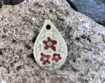 May include: A teardrop-shaped ceramic pendant with a light green glaze and three pink flowers.