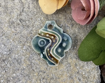 May include: A ceramic pendant with a blue, green, brown, and white abstract design. The pendant has a hole at the top for hanging.