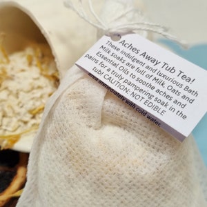 May include: A white muslin bag filled with a bath soak mix. The bag has a white label that reads "Aches Away Tub Tea! These indulgent and luxurious Bath Milk soaks are full of Milk, Oats and Essential Oils to soothe aches and pains for a truly pampering soak in the tub! CAUTION: NOT EDIBLE area immediately with cold water."