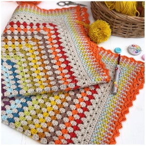 May include: A colorful crochet blanket with a rainbow pattern and a scalloped edge. The blanket is made with a variety of colors, including red, orange, yellow, green, blue, and purple. The blanket is folded in half and is lying on a white surface. The text "@sewhappycreative" is visible on the blanket.