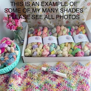 May include: A Lucky Dip Yarn Box containing multiple skeins of variegated pastel yarn with white labels, a light blue bowl filled with small yarn bundles, a crochet hook with a floral handle, and a multicoloured chevron-patterned crochet blanket.