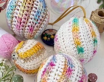 Op de afbeelding: Vier kleurrijke gehaakte kerstballen met wit garen en meerkleurige strepen. De ballen zijn versierd met gouden glitter.