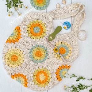 Puede incluir: Un bolso de mano de crochet con un dise&ntilde;o de girasol en tonos amarillos, verdes y crema. El bolso tiene una sola correa y est&aacute; hecho con un punto de granny square.