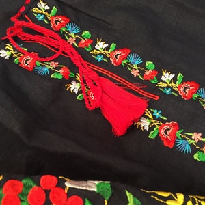 May include: Black linen fabric with red, white, blue, green, and yellow embroidered flowers and berries. The fabric has a red tassel.