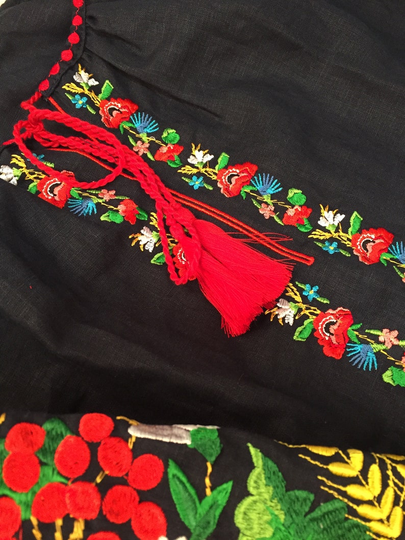 May include: Black linen fabric with red, white, blue, green, and yellow embroidered flowers and berries. The fabric has a red tassel.