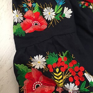 May include: Close-up of a navy blue fabric with embroidered red poppies, white daisies, green leaves, and yellow stems.