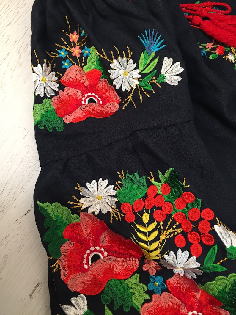 May include: Close-up of a navy blue fabric with embroidered red poppies, white daisies, green leaves, and yellow stems.