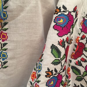 May include: White linen fabric with colorful embroidered floral designs. The embroidery features pink, blue, red, yellow, and green flowers with black outlines.