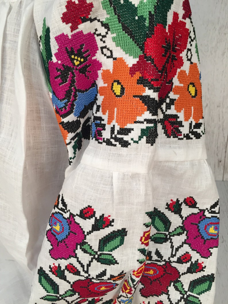 May include: White linen blouse with colorful embroidered floral patterns on the sleeves. The embroidery features red, orange, yellow, green, blue, and pink flowers.