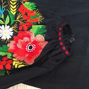 May include: A black linen blouse with red and green embroidered flowers. The embroidery is detailed and intricate, featuring a variety of floral motifs.