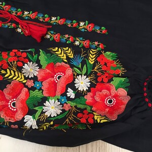 May include: Black embroidered blouse with red, white, yellow, and green floral embroidery. The embroidery features poppies, daisies, and wheat.