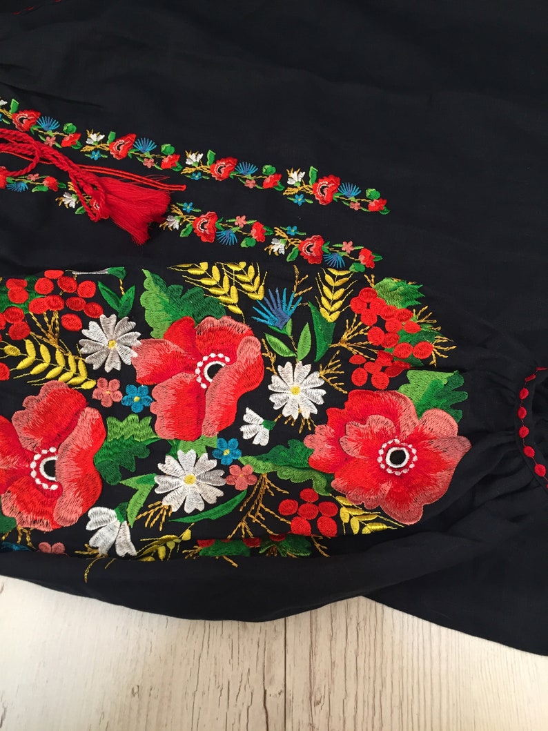 May include: Black embroidered blouse with red, white, yellow, and green floral embroidery. The embroidery features poppies, daisies, and wheat.