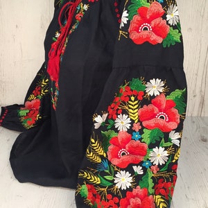 May include: A black embroidered blouse with red, white, and green floral designs. The embroidery features poppies, daisies, and wheat stalks.