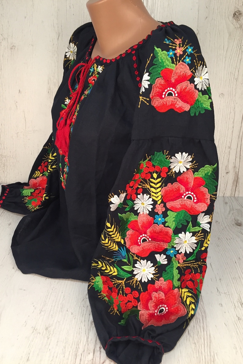May include: A black embroidered blouse with red, white, and green floral designs. The embroidery features poppies, daisies, and wheat stalks.