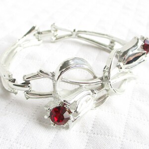Puede incluir: Pulsera de metal plateado con dise&ntilde;o floral. Presenta tres elementos en forma de tulip&aacute;n, cada uno con una gema roja vibrante. La pulsera articulada parece estar hecha de metal ligero.
