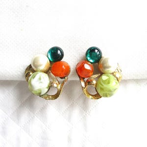 May include: A pair of vintage clip-on earrings. Each earring has a cluster of colourful beads in green, orange, white, and green-swirled. The beads are set on a gold-tone metal base with a leaf design. The earrings are on a white background.