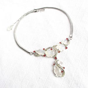 Op de afbeelding: Een zilveren ketting met een witte en rode bloemenhanger. De hanger heeft gesneden witte bloemen met rode strass-accenten.