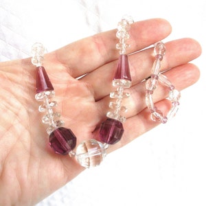 May include: A vintage necklace with clear and amethyst glass beads. The necklace features alternating clear and amethyst beads, with larger amethyst beads at the center.