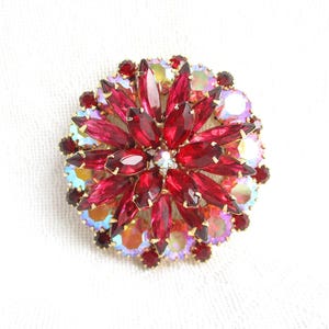 May include: A vintage brooch with a floral design. The brooch features a central cluster of deep red, marquise-cut rhinestones surrounded by smaller, round red and iridescent stones. The setting is gold-toned.