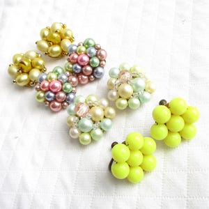 May include: A collection of vintage clip-on earrings in various styles and colors. Some earrings feature clusters of faux pearls in shades of yellow, pink, blue, and green. Other earrings are bright yellow, with a cluster of round beads.