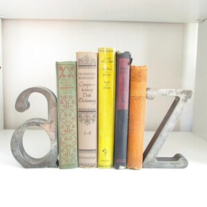 Könnte beinhalten: Ein metallenes A-Z-Buchstützen-Set, das eine Reihe von Vintage-Büchern hält. Die Bücher haben verschiedene Farben und Designs, darunter Grün, Gelb und Orange. Die Buchstützen sind aus silberfarbenem Metall.