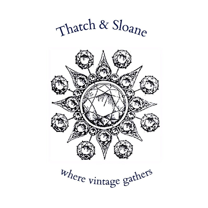 Puede incluir: Ilustraci&oacute;n en blanco y negro de un dise&ntilde;o de joyer&iacute;a circular con una gran gema central rodeada de gemas m&aacute;s peque&ntilde;as. El texto "Thatch & Sloane" est&aacute; arriba y "where vintage gathers" abajo.