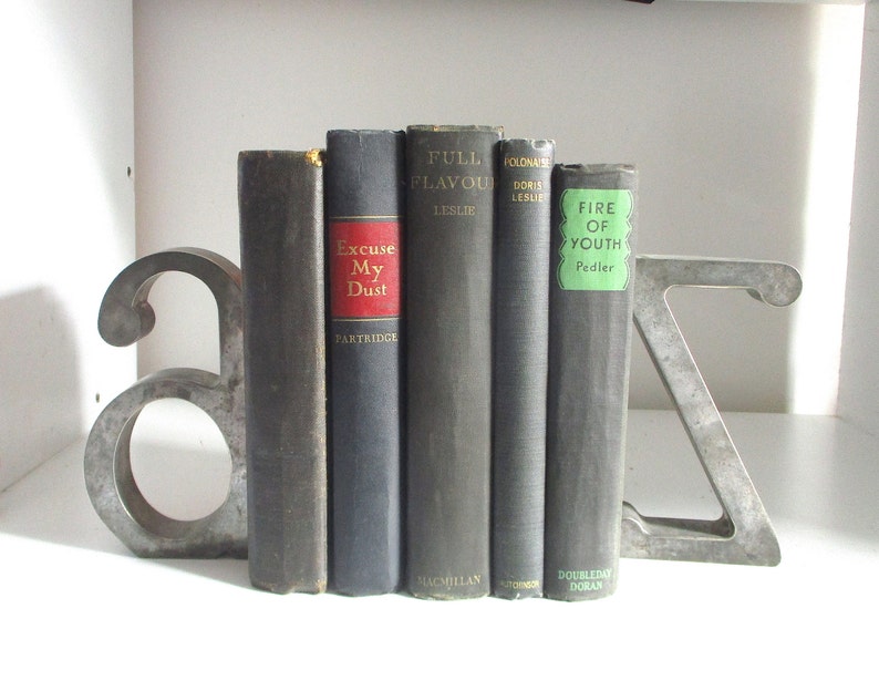 May include: A set of bookends shaped like the letters A and Z, made of metal, holding up a row of five hardcover books with titles including "Full Flavour", "Polonaise", "Excuse My Dust", and "Fire of Youth".