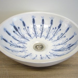 Könnte beinhalten: Ein weißes Keramik-Waschbecken mit einem blauen Blumendesign. Das Waschbecken ist rund und hat einen Abfluss in der Mitte.