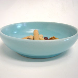 Könnte beinhalten: Eine hellblaue Keramikschüssel mit glatter, glänzender Oberfläche. Die Schüssel ist mit einer kleinen Menge an Snacks gefüllt, darunter Cracker, Nüsse und Trockenfrüchte.