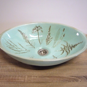 May include: A light blue ceramic sink with a drain and a design of brown pressed botanicals.