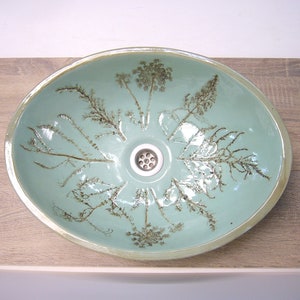 May include: A light blue ceramic sink with a brown floral design. The sink has a round drain in the center.