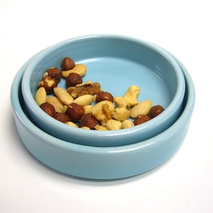 Könnte beinhalten: Zwei hellblaue Keramikschalen, die ineinander gesteckt sind, gefüllt mit verschiedenen Nüssen, darunter Mandeln, Haselnüsse und Cashews.