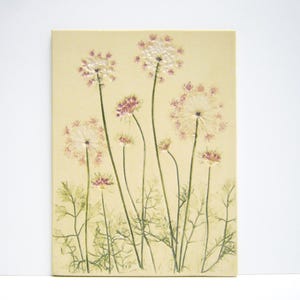 May include: A cream-coloured card with a pressed flower design. The flowers are white with pink accents and are arranged in a vertical line. The card is blank and ready for a message.