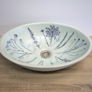 May include: A white oval ceramic sink with a black floral design and a silver drain.
